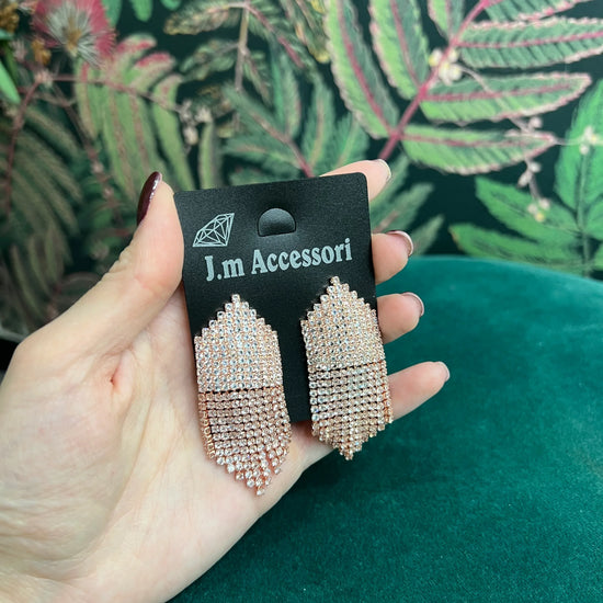 Hand holding J.m Accessori card displaying pink rhinestone drop earrings against green patterned background