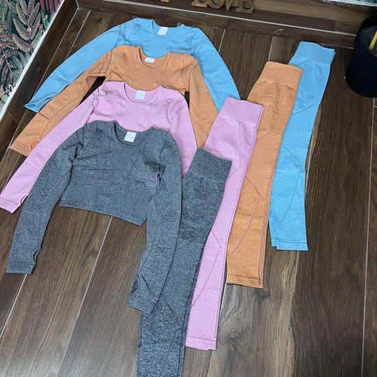 Four colorful SPORT 08 seamless long sleeve crop tops and matching leggings laid out on wooden floor.