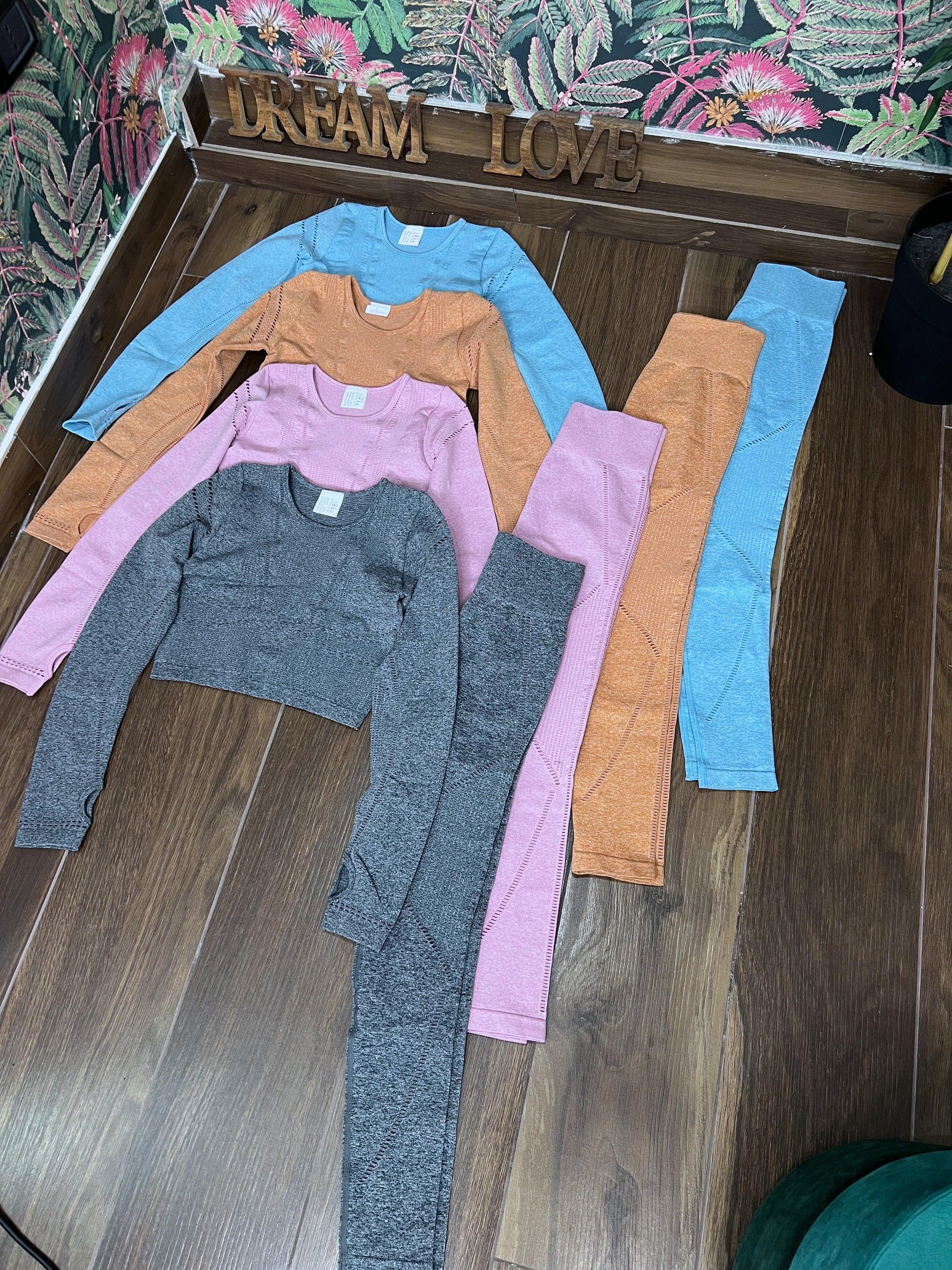 Four colorful SPORT 08 seamless long sleeve crop tops and matching leggings laid out on wooden floor.