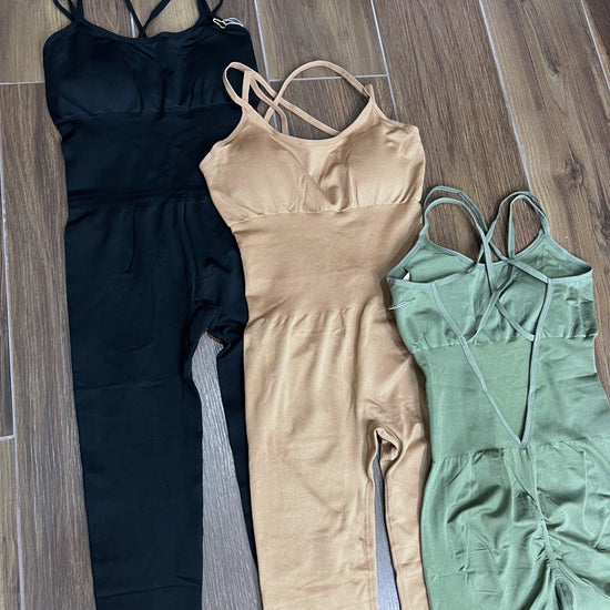 Three SPORT 03 sleeveless fitted jumpsuits in black, beige, and green laid on wooden floor.
