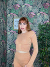 Woman wearing a fitted tan long-sleeve crop top and matching high-waisted leggings against floral wallpaper background