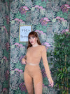 woman wearing tan long sleeve crop top and leggings set posing against floral wallpaper background