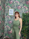 woman wearing green SPORT 03 athletic jumpsuit standing against floral patterned wall with indoor plants