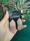 Hand holding rose gold sparkly chandelier earrings on black J.m Accessori card with green floral background