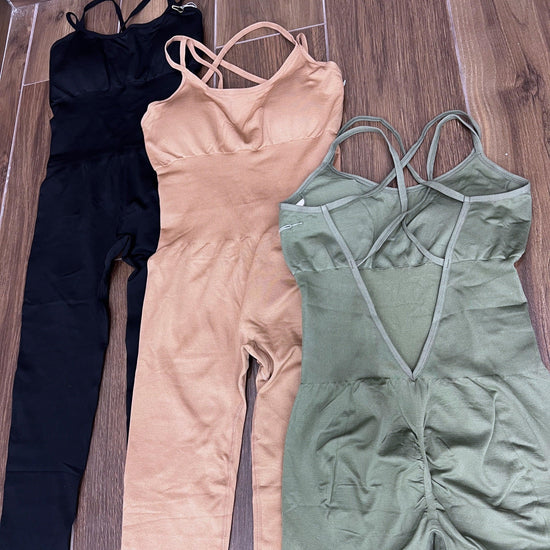 Three SPORT 03 sleeveless workout jumpsuits in black, beige, and olive green laid flat on wooden floor.