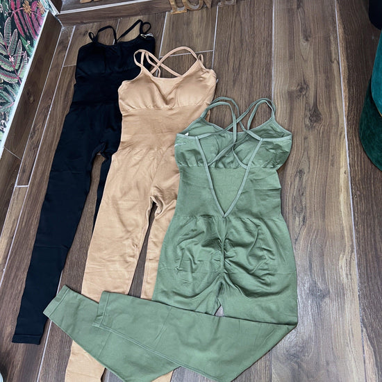 Three SPORT 03 women's one-piece athletic jumpsuits in black, beige, and olive green laid on wooden floor