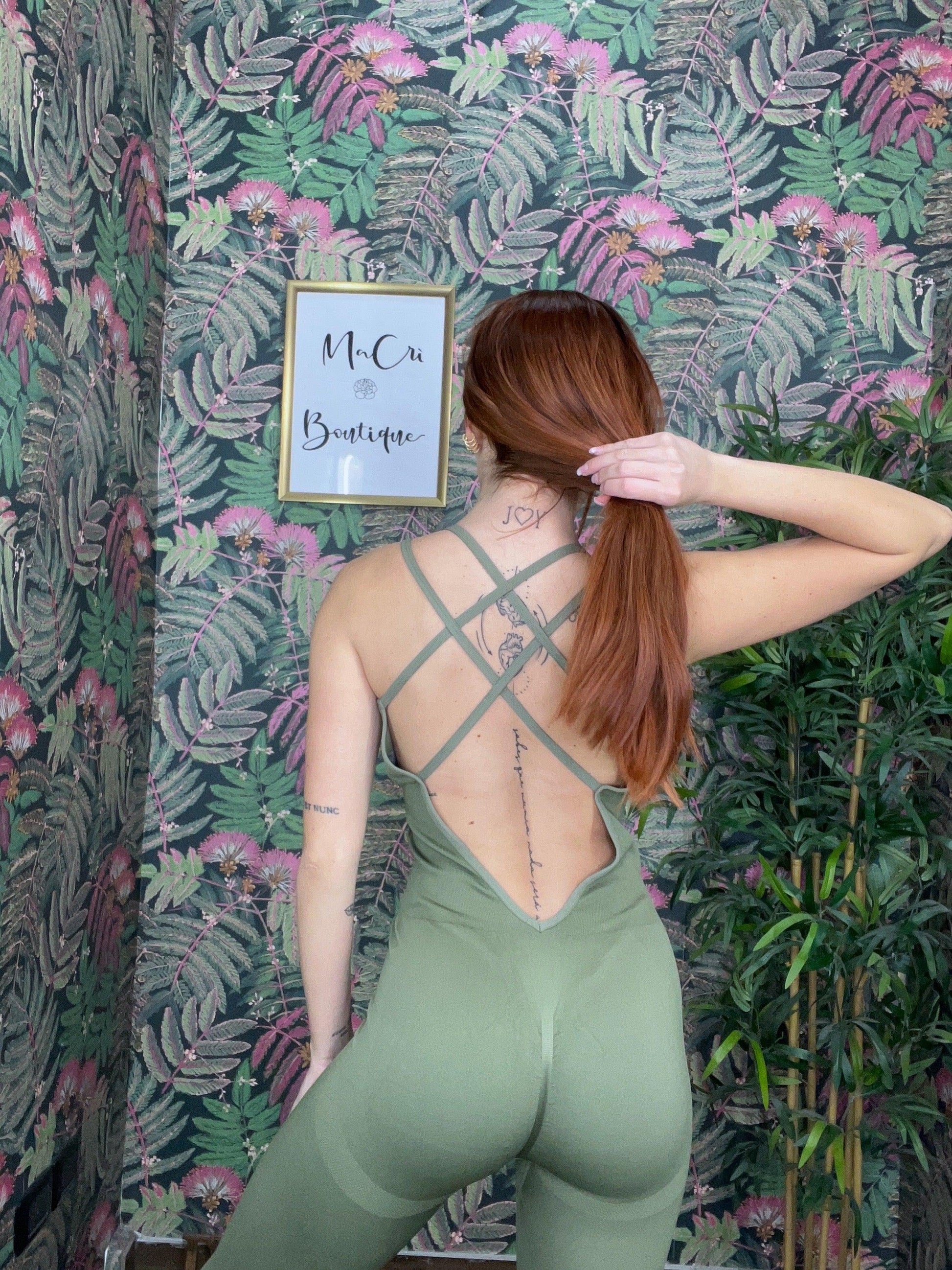 woman wearing green crisscross back SPORT 03 activewear against floral wallpaper in boutique setting