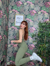 woman wearing olive green SPORT 03 activewear outfit posing against tropical floral wallpaper background