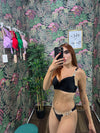 Woman taking mirror selfie wearing black bikini with gold chain details against floral wallpaper background
