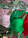 Three colorful bikini tops with jeweled straps hanging on white hangers against a floral background