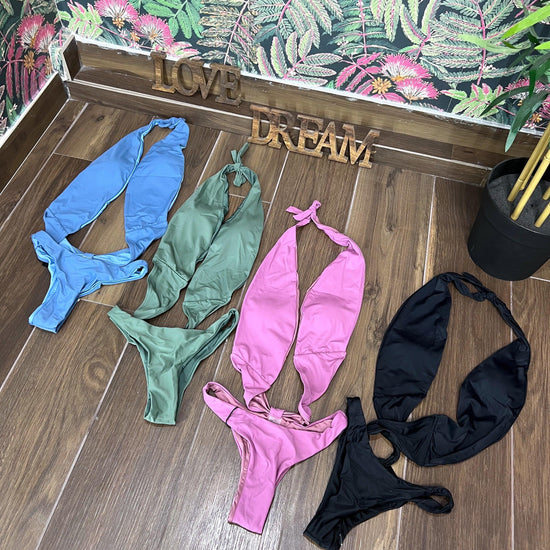 Four trikini swimsuits in blue, green, violet, and black laid out on a wooden floor with floral wallpaper background.