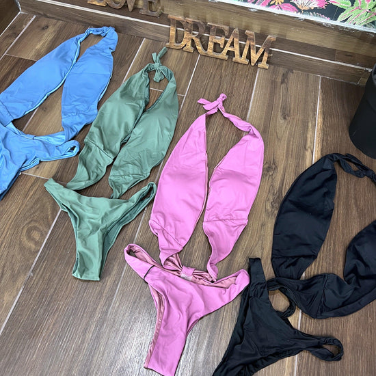 Four stylish trikinis in blue, green, violet, and black laid out on wooden floor with decorative love and dream signs.