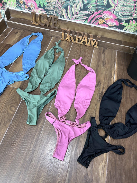 Four stylish trikinis in blue, green, violet, and black laid out on wooden floor with decorative love and dream signs.
