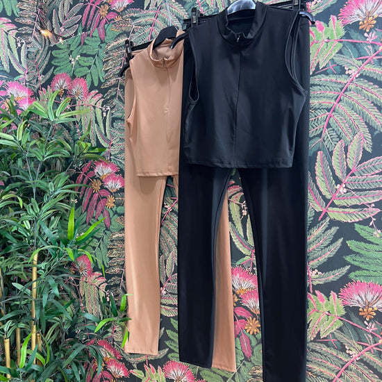 Two sleeveless fitness outfits in black and beige hanging against a floral patterned wall background