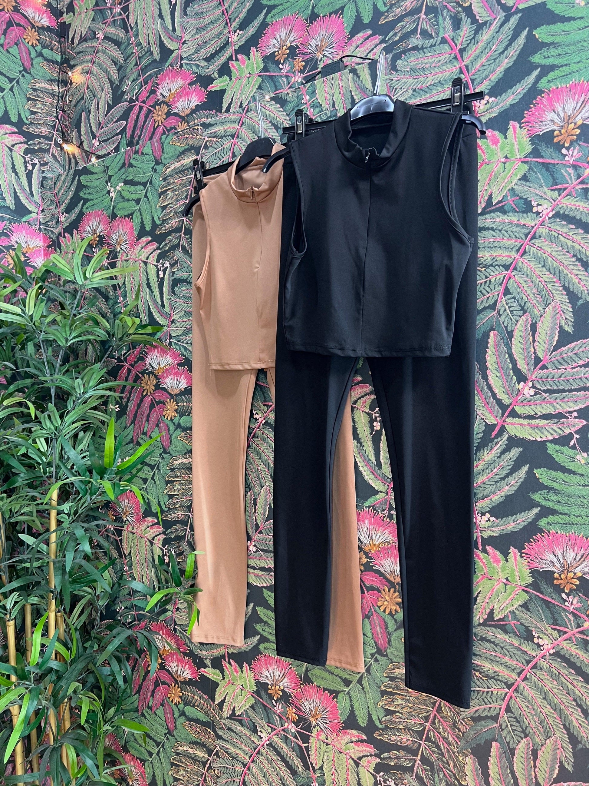 Two sleeveless fitness outfits in black and beige hanging against a floral patterned wall background