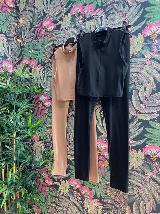 Two sleeveless fitness outfits in black and beige hanging against a floral patterned wall background