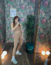 Woman taking mirror selfie wearing tan coordinated fitness outfit with light blue sneakers in floral wallpaper room
