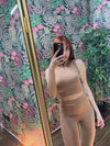 Woman taking a mirror selfie wearing a beige sleeveless crop top and high-waisted leggings fitness outfit indoors